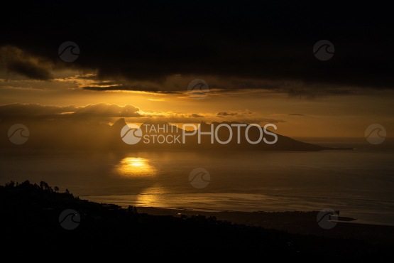 Soleil couchant orangé sur Moorea, sous ciel nuageux